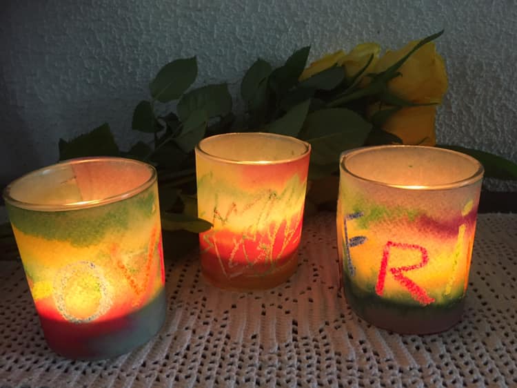 3 lys i fargerike kopper med noen gule roser bak